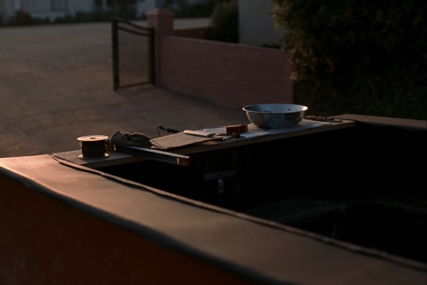 An open truck tailgate used as a workbench in a driveway at golden hour: a spool of wire, a level, work gloves and a clipboard.