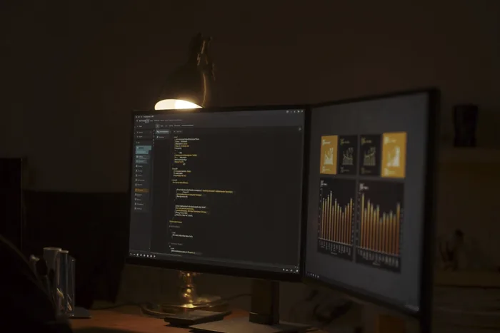 Two monitors on a dark desk, code on one and a dashboard on the other.
