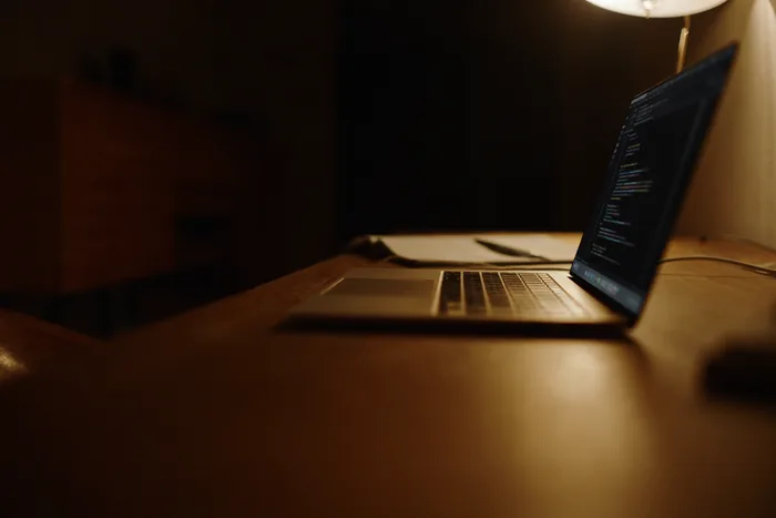 A laptop open on a dark desk showing a terminal session, warm light from one side.